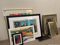 Four framed artworks, ornate frame, and multiple empty frames grouped against wall