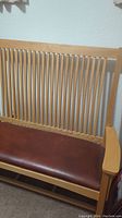 Close-up of the wooden slatted backrest and brown leather seat cushion of the bench chair.