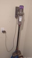 Full view of vacuum mounted on wall with charging dock and cord plugged in