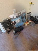 Various electronic items arranged on carpet showing all included pieces together including Mepro 88 projector, Belkin iPod kit, joystick controller, and cables.