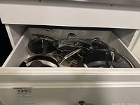 Drawer overview showing multiple stainless steel pans, lids and one nonstick pan