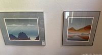 Both framed art prints hanging on wall, blue-green and orange landscapes