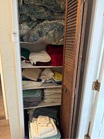 Closet shelves stacked with neatly folded assorted linens including towels, sheets, pillowcases, blankets, and pillows visible at top.