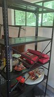 Full view of black metal shelving with items arranged on several shelves including red toolbox containers and various tools.