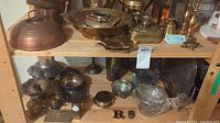 Shelf with various metal serveware items including kettles, bowls, candle holders, trays, and small containers.