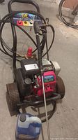 Full view of Honda pressure washer unit with frame, wheels, hose, wand, and solution jug