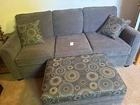 Front view of three-seat grey sofa bed with patterned ottoman and two matching cushions