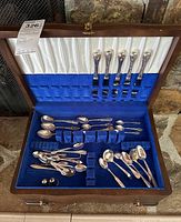 Top-down view of open wood chest showing EP plated knives in lid loops and various spoons in velvet tray