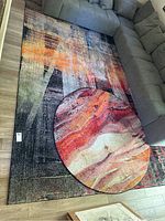 Rectangular and round rugs positioned together under sofa showing overall abstract design and scale.