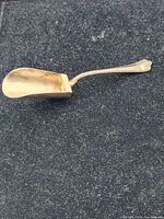 Side view of the silver sugar spoon showing the deep scoop-shaped bowl and ornate handle on a dark textured background.