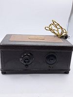 Front view of the Atwater Kent antique radio showing two tuning and volume dials, with twisted fabric power cord attached.