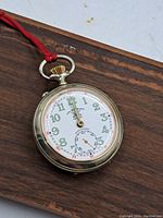 Front view of pocket watch on wooden surface showing full enamel dial, crown, bow, and case profile