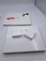 MacBook laptops and their power adapters on white surface, showing top view of keyboards and closed lid with stickers.