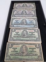 Overview of seven Canadian banknotes from 1937 in used condition arranged in a tray containing $1, $5, and $10 denominations.