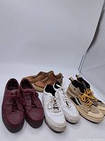 Four pairs of men's shoes including maroon sneakers, tan boots, white Adidas sneakers, and beige high-top sneakers on white backdrop.