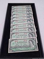 Ten Canadian $1 Centennial bills arranged overlapping in a tray, showing the front side featuring Queen Elizabeth II portrait and text.