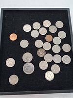 Various US coins laid out on black background showing assortment of pennies, nickels, dimes, quarters, half dollar, and dollar coin