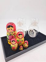 Image showing the vintage Russian Matryoshka nesting dolls of five sizes along with three clear glass nesting figurines, placed on a black surface.