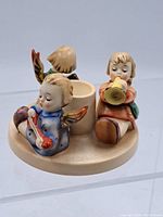 Front and side view of the M.I. Hummel Herald Angel Candleholder showing the three angel figurines seated around the candle cup.