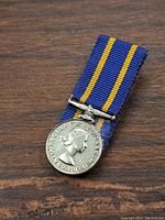 Front view of miniature medal hanging from blue and yellow ribbon showing Queen Elizabeth II profile.