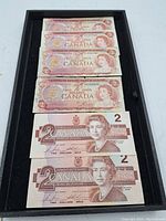 Six Canadian $2 banknotes displayed flat, including four older vintage notes and two newer 1986 notes, showing the front side with Queen Elizabeth II portraits and legal tender text.