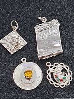 Top view of four sterling silver charms showing detailed designs and textures.