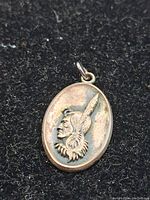 Front view of oval sterling silver pendant showing detailed First Nations style head in feathered headdress in relief on black background.