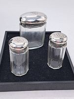 Overview of three antique glass dresser bottles with sterling silver lids monogrammed with script initials
