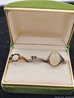 Opened jewelry box containing three vintage rings: one with a large oval cabochon gem, a silver ring with small clear stones, and another gold open-design ring.