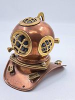 Front angle view of miniature diver's helmet showing copper body with brass window grilles and fittings