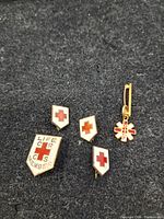 Four vintage Red Cross pins on dark fabric background showing overall condition and details