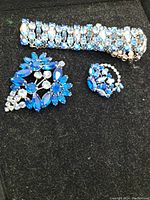 Set of vintage rhinestone costume jewelry on black felt showing the bracelet, brooch and one clip-on earring.