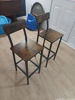 Front/right angled view showing wooden seat and backrest with metal frame and legs for two chairs, situated in a room with light wood floor.