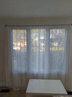 Wide shot of a window covered with one pair of sheer curtains showing vertical subtle stripes with light through the fabric