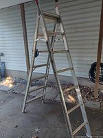 Full view of ladder set up in step-ladder position showing aluminum frame, wide steps, and red foot caps.