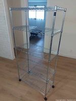 Full view of chrome shelving unit with five wire shelves. The unit has a sturdy metal frame and four black caster wheels for mobility. The shelves are evenly spaced and made of metal wire mesh with adjustable clips on poles.