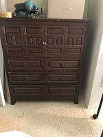 Front view of vintage 1970s tall dresser showing closed drawers and top cabinet doors with decorative metal pulls.