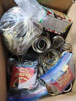 Box containing a plastic bag with multiple jar lids and seals, along with other packaged items and jars.