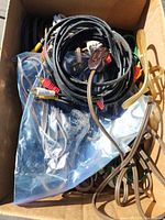 Box containing various vintage extension cords including black and brown cords with on/off switches and standard plugs, some loose and some bundled.
