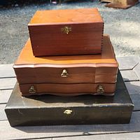 Three wooden boxes stacked: a flatware box on the bottom, a smaller wooden box in the middle, and a cigar box at the top.