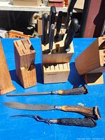 Photo of three wooden knife blocks with various knives, some with black handles, some with antler-style handles, laid on blue surface.
