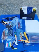 Office supplies spread on blue surface, including pens, pencils, scissors, notebooks, and organizers.