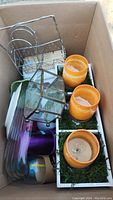 Overview of kitchenware and decor items in a cardboard box, showing candle holders, wire basket, and glass containers