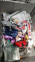 Image of miscellaneous toys, action figures, a plastic blue vehicle, a red toy vehicle, and various collectible items including a No Smoking sign and comic book slip covers in storage bin.