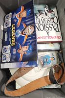 Top view of the bin containing NHL Legends hockey card box, book titled 'Passion Served' by George Jones, past player memorabilia cards in plastic case, and a leather belt.