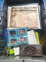 Top view of bin contents showing copper plate, decorative wooden box, four copper-colored bells in packaging, framed papers or magazines underneath