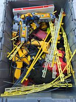 Top view of bin containing numerous toy cars, track pieces, remote controller device, wires, and other toy parts