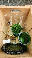 Close-up of the glass candle holders, green vases, oil lamp, ashtray, miniature elephant figurine, and small box inside a wooden crate.