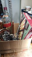 Box with a large empty Johnnie Walker bottle with wooden holder, visible backgammon board box, and tangled electrical cords.