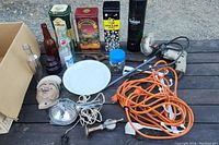 Collection of collectable tins, vintage bottles, electric buffer, extension cord, Pyrex plate, and other miscellaneous items spread on dark wooden surface.